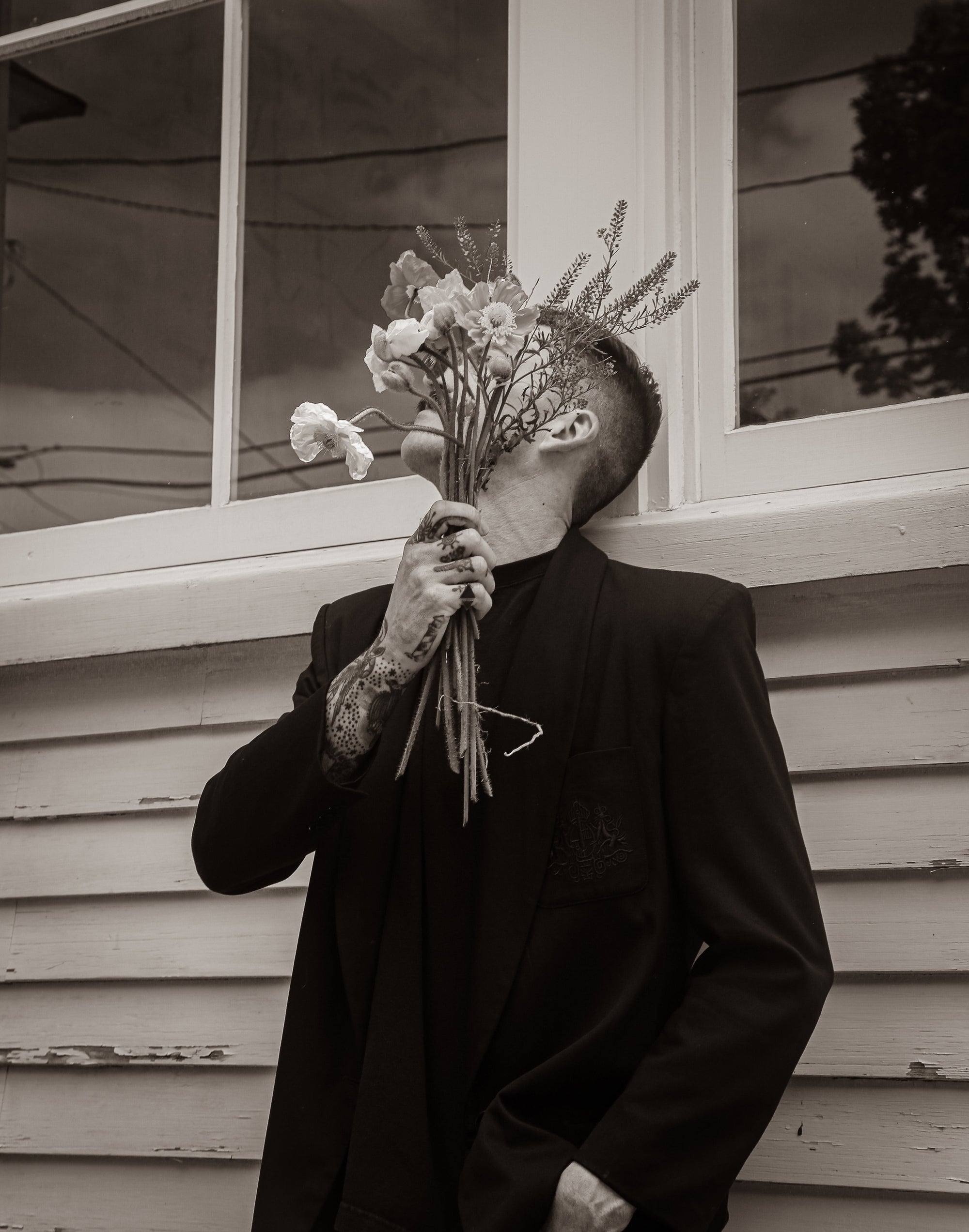 A black and white image of a man holding flowers in front of his face