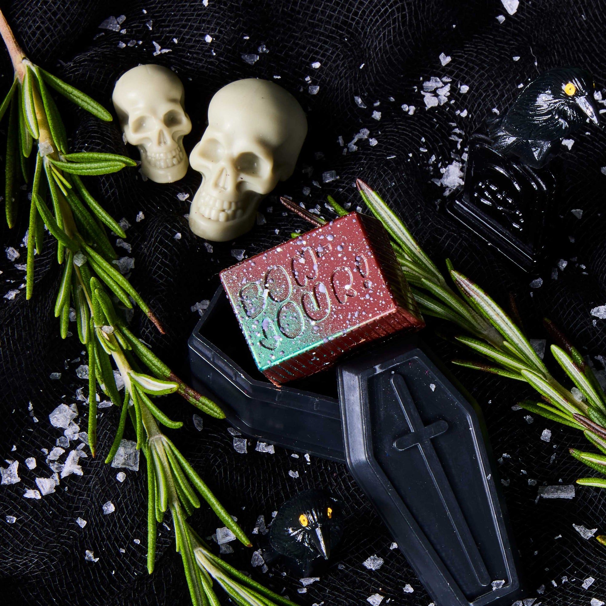 Olive Oil & Sea Salt Bon on a black coffin, with skulls and rosemary in the background.