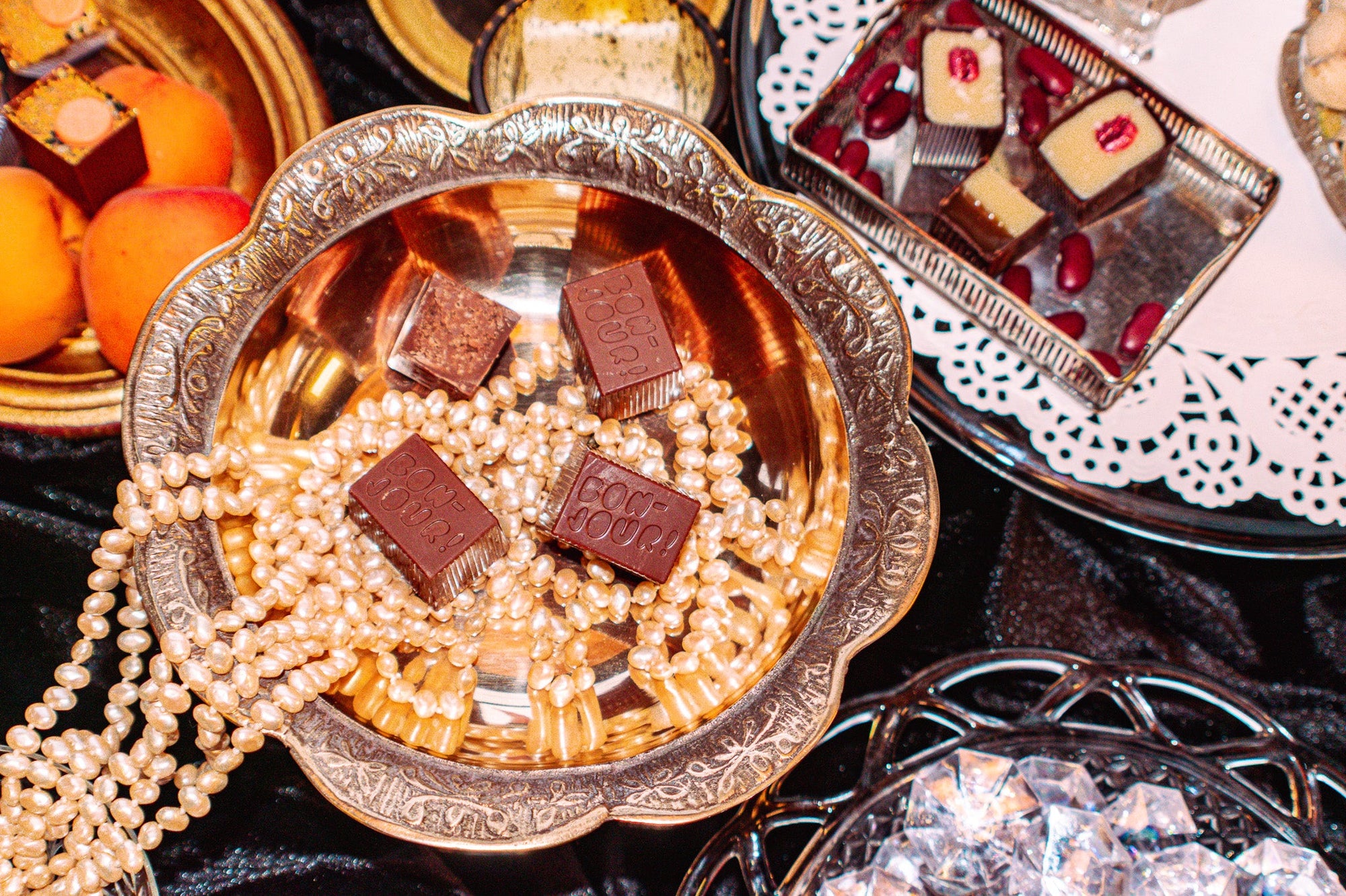 Pearl necklaces in a tin chalice with four Bons on top. Half of some of the necklaces are pouring out. Sat on a table with other bons in the background.