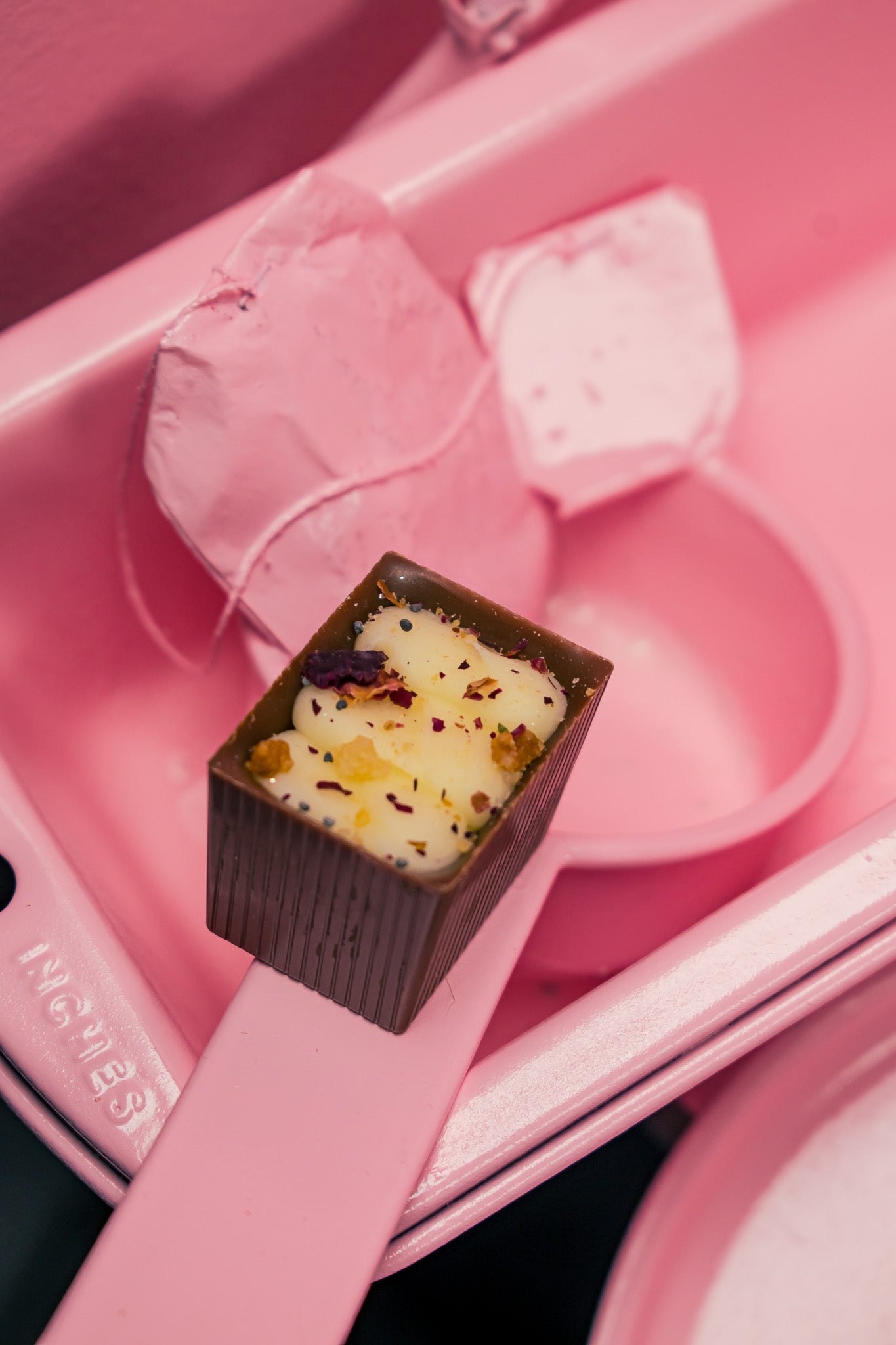 Bon resting on pink measuring cup with a pink tea bag beside it. All is sitting in a pink cake tin.