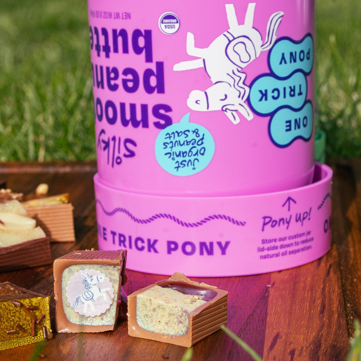 Purple One Trick Pony cup of peanut butter and three Bons on a wooden board in the grass