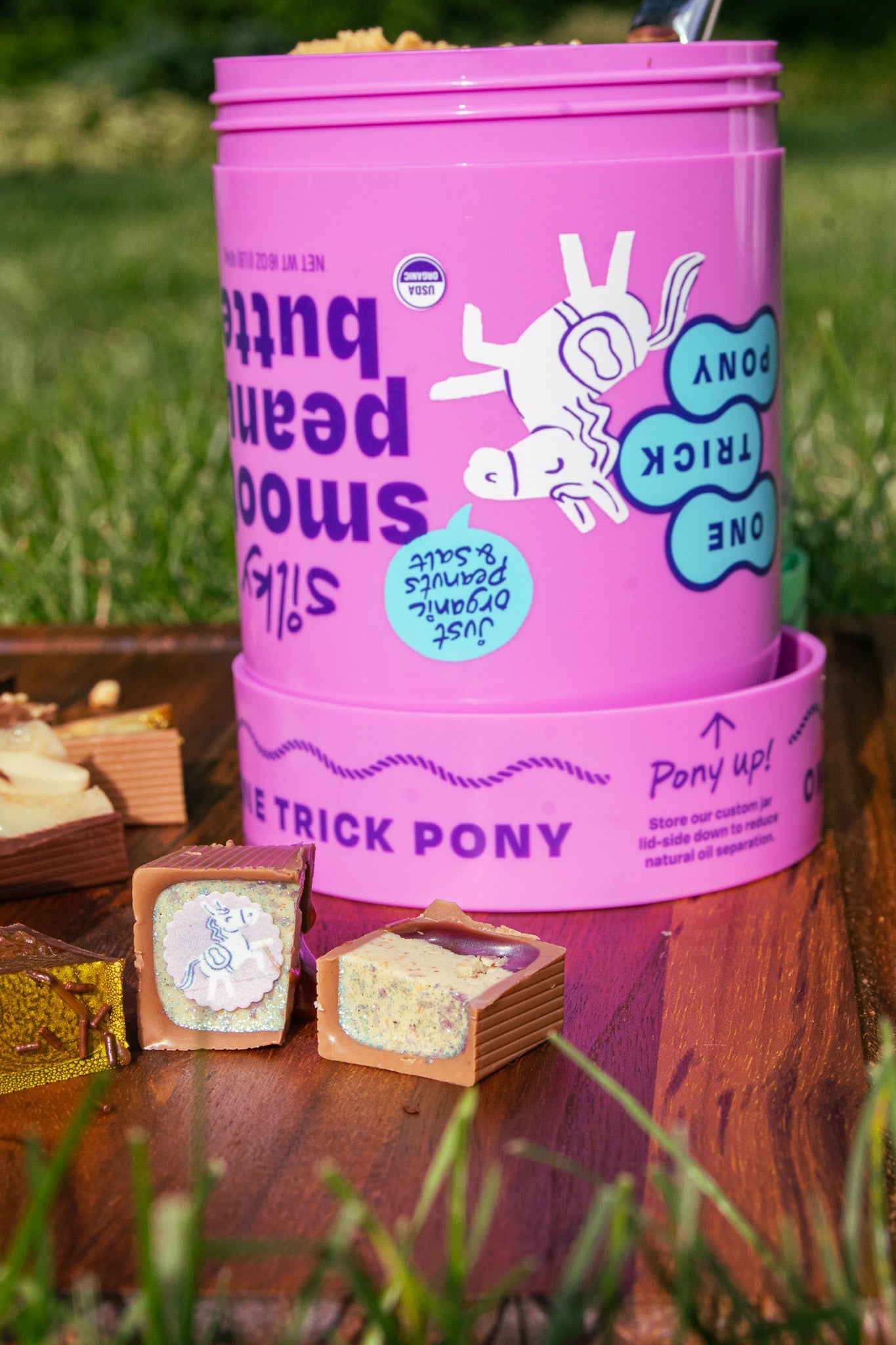 Purple One Trick Pony cup of peanut butter and three Bons on a wooden board in the grass