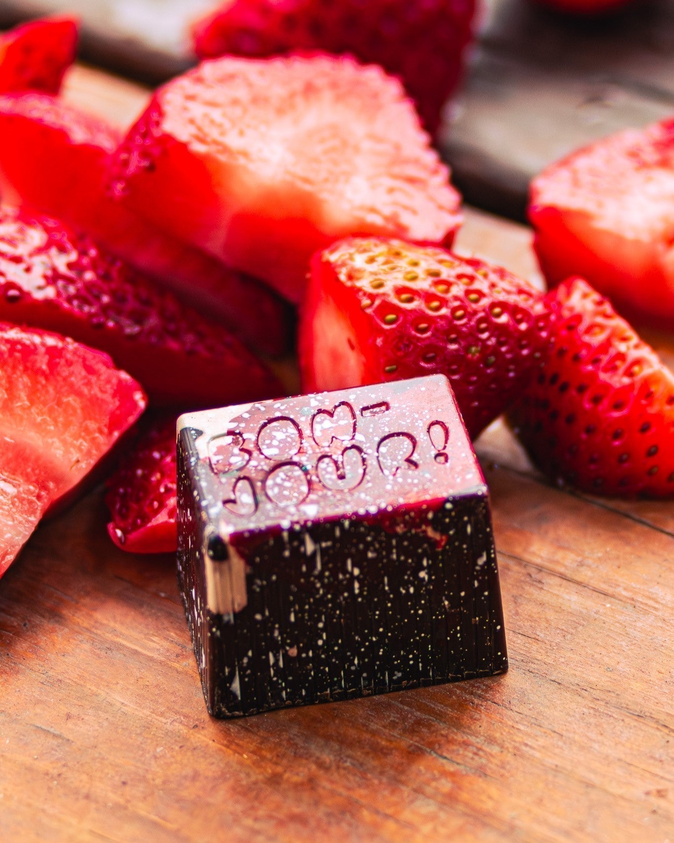 Bon on a wood table with cut strawberries in the background.