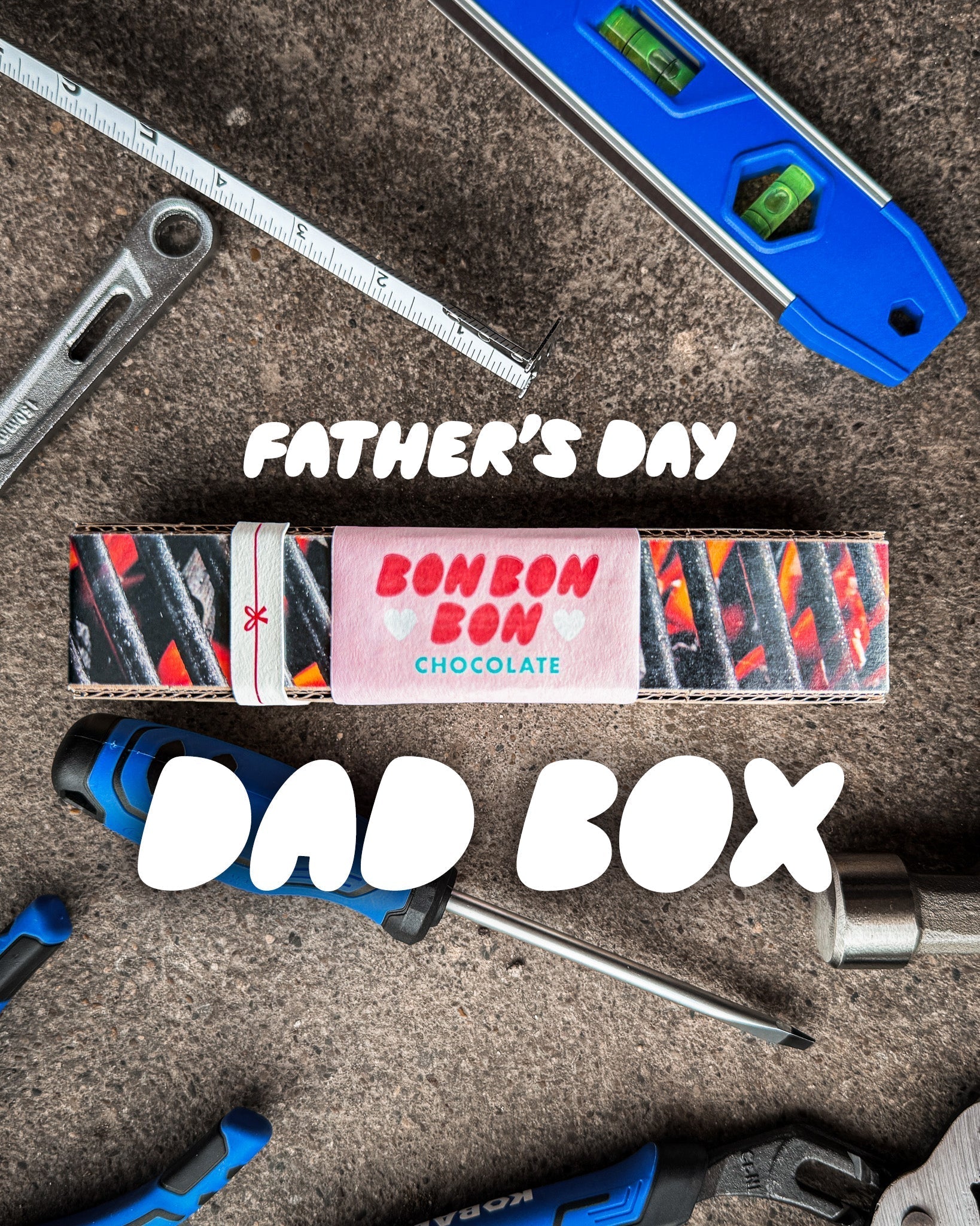 Concrete floor with general tools around and a box of chocolates. Text overlaying saying "Father's Day" and "Dad Box"