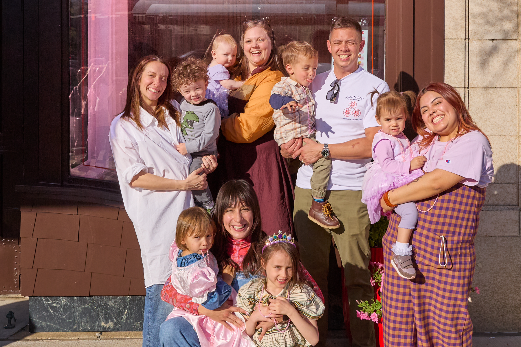 Four women and one man all holding children in front of store.