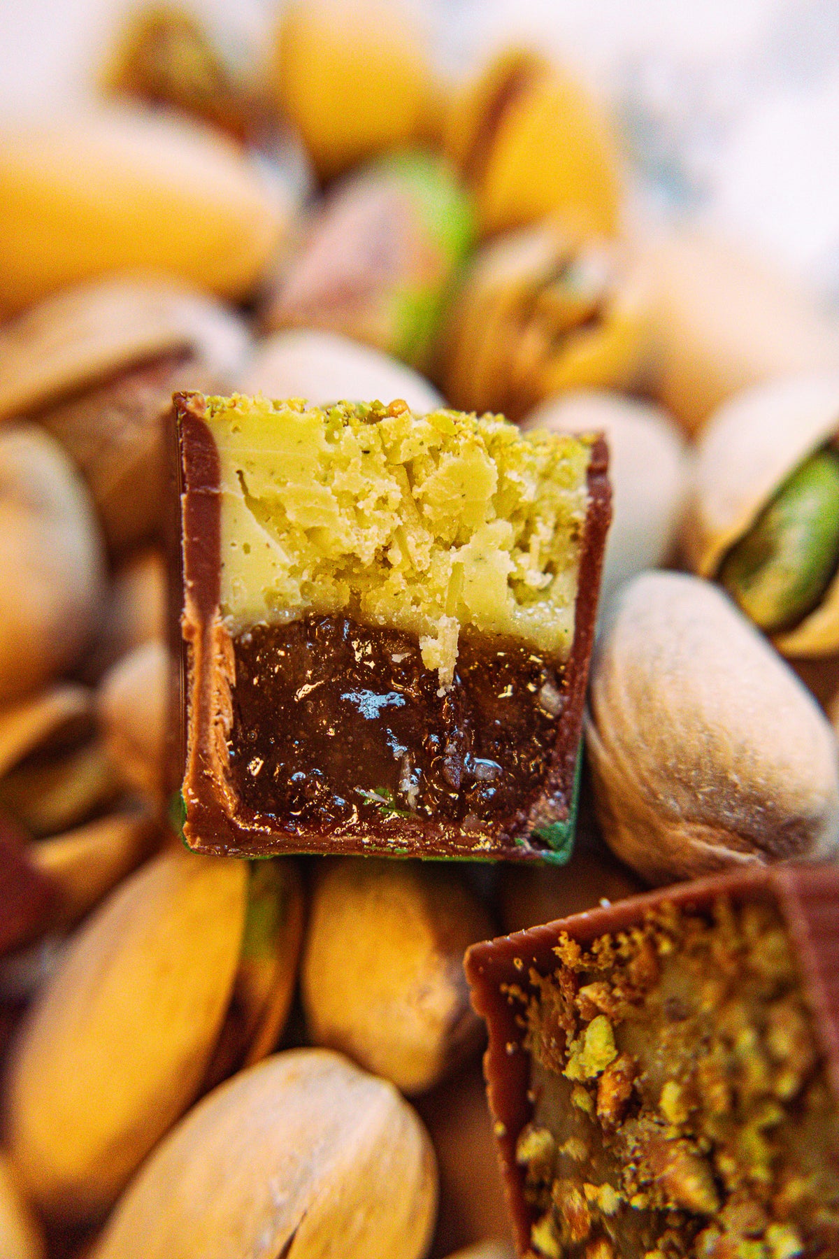 Can’t Get Künefe Bon Bon Bon — a milk chocolate bon bon filled with rosewater & tart apple sweet cheese pastry and pistachio crumb for Bon Bon Bon's 2026 Valentine's Day Proper Fancy Collection. The bon bon is pictured cut in half on a bed of pistachios.