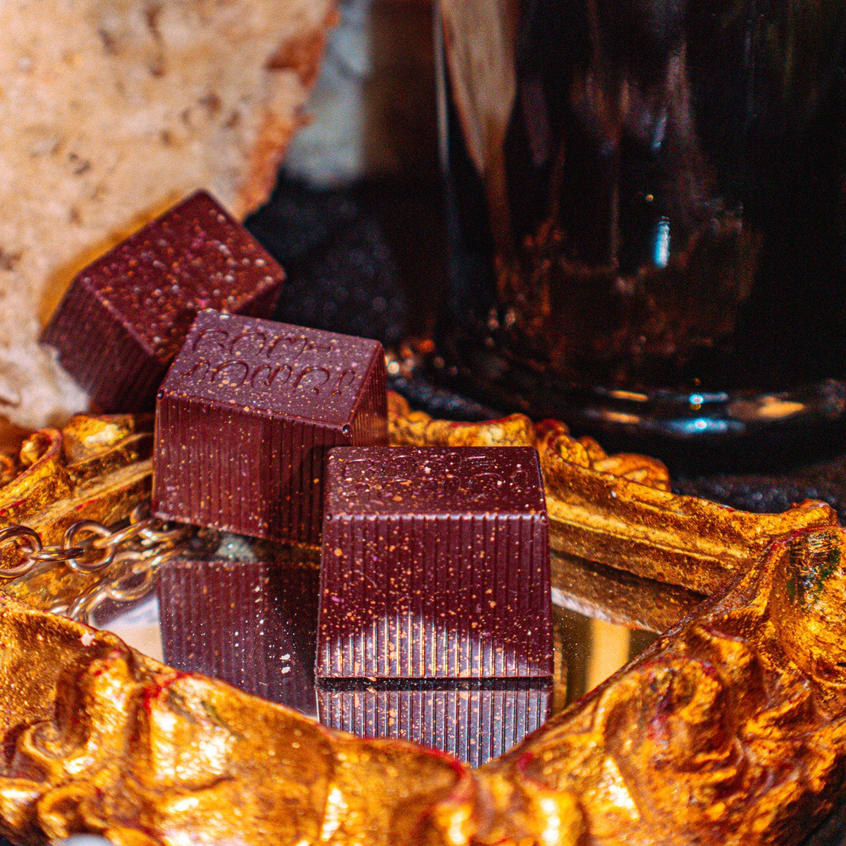 Champagne Toast Bon Bon Bon — a dark chocolate bon bon filled with sparkling wine caramel and sourdough crumb for Bon Bon Bon's 2026 Valentine's Day Proper Fancy Collection. The bon bons are pictured sitting on a fancy gold mirror.