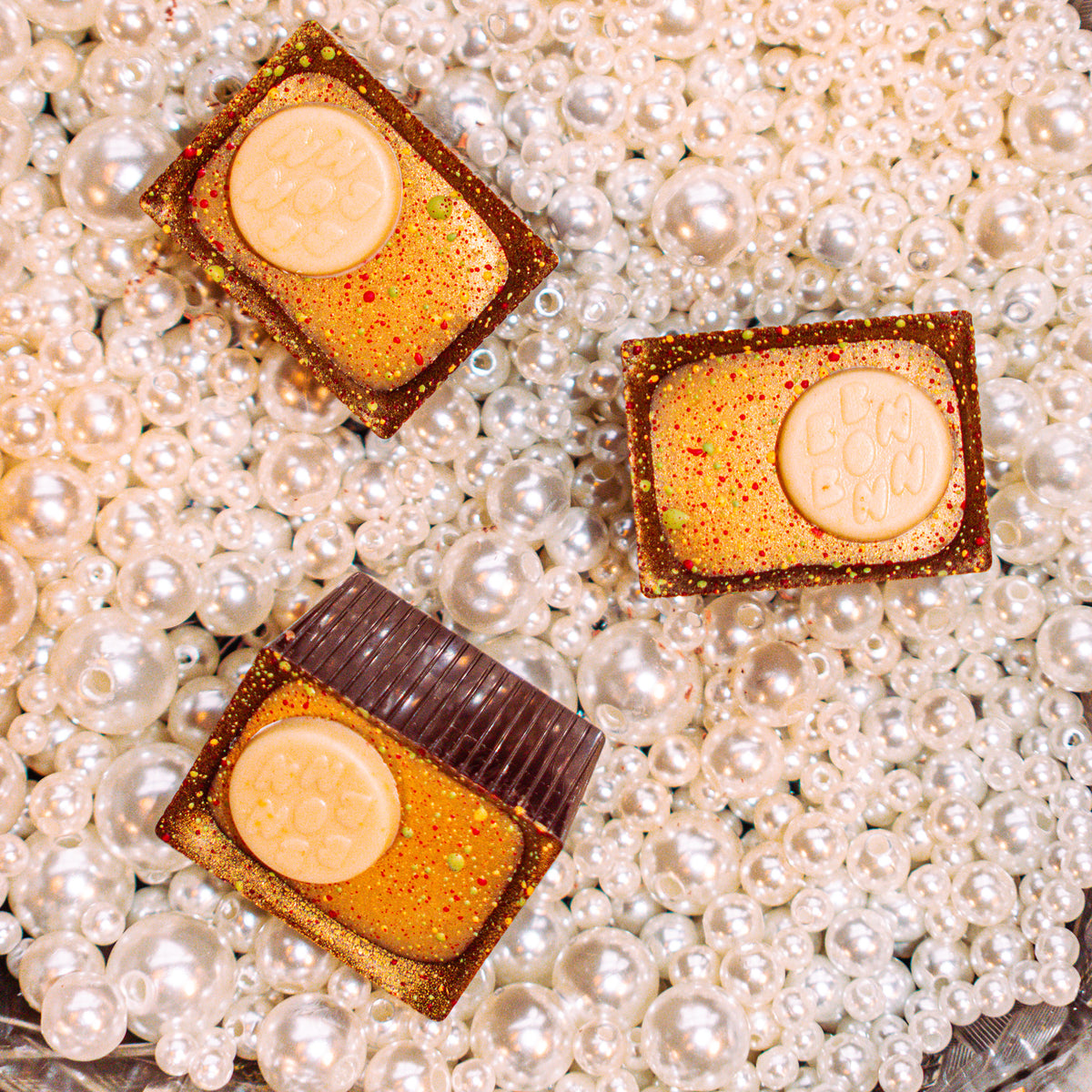 Paw Paw Panettone Bon Bon Bon — a dark chocolate bon bon filled with candied citrus panettone ganache and paw paw confiture for Bon Bon Bon's 2026 Valentine's Day Proper Fancy Collection. The bon bons are pictured sitting in a bed of pearls.