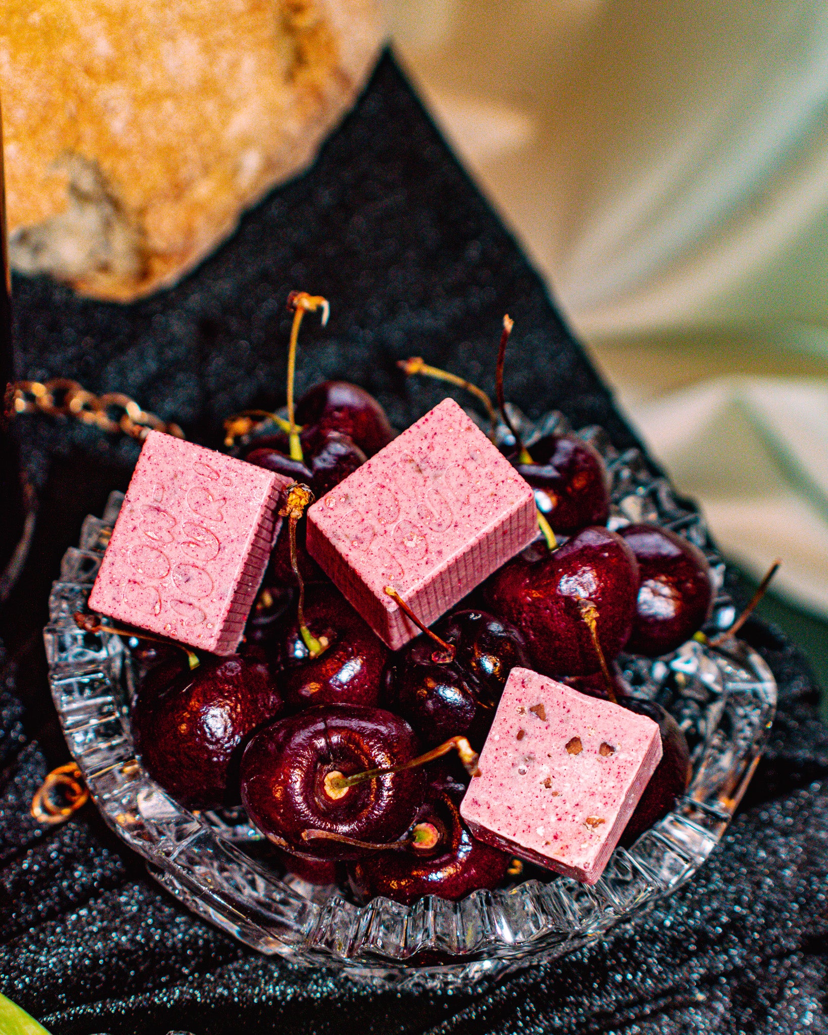 Pit-iful Bon Bon Bon — a sour cherry infused white chocolate bon bon studded with candied nibs, vanilla bean and meringue chunks for Bon Bon Bon's 2026 Valentine's Day Proper Fancy Collection. The bon bons are pictured on a bed of cherries in a fancy glass dish.