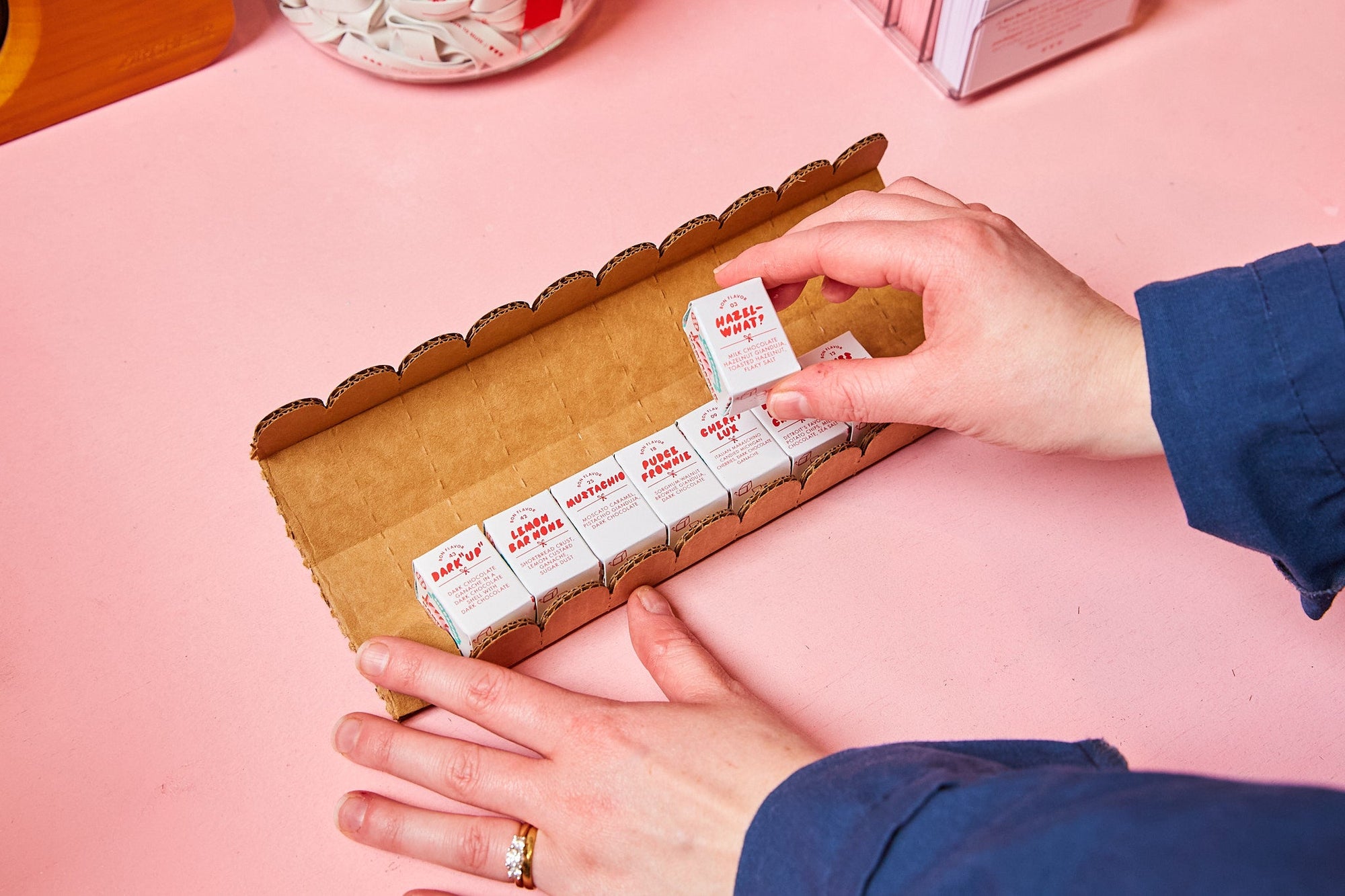 Person arranging small boxes with red labels on a pink surface