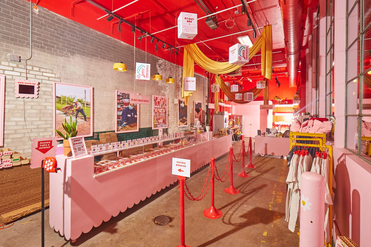 The view of Bon Bon Bon's shop in Midtown, Detroit, as seen from when you first walk in the door. The store features a pink counter with scalloped edges, cute signage and photography of the chocolate being made, and giant Bon cartons hanging from the ceiling.