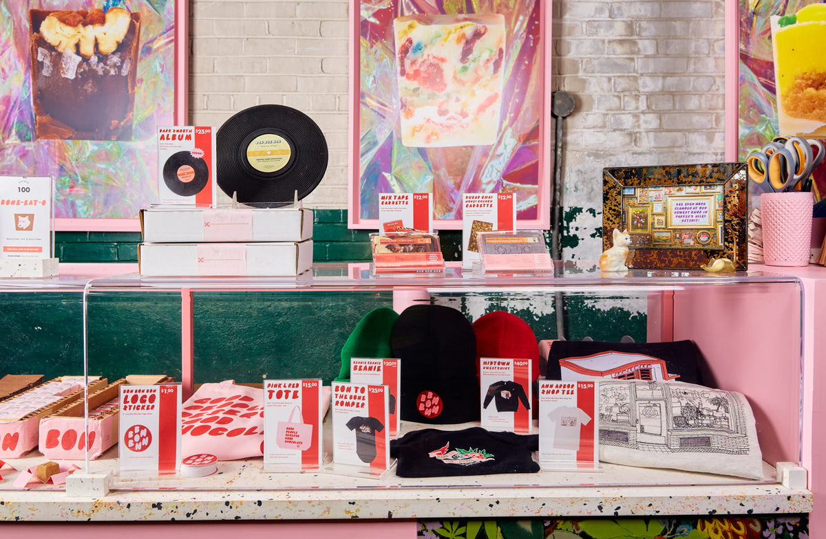 A close up of the counter at Bon Bon Bon's shop in Midtown Detroit, showcasing their apparel and merchandise as well as chocolate novelties such as a vinyl album made of chocolate