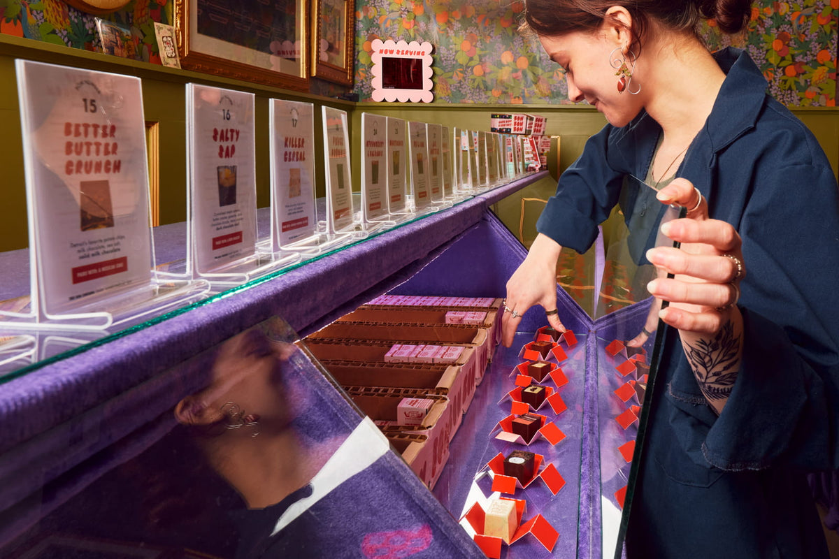 A retail employee taking a chocolate bon bon out of the display case at Bon Bon Bon's Parker's Alley Detroit location.